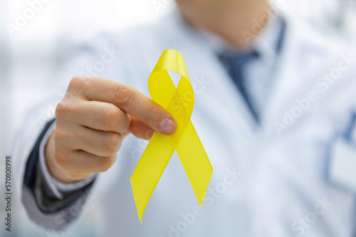Stampa su tela Doctor in a white uniform holds a yellow ribbon in his hand, symbol of the fight