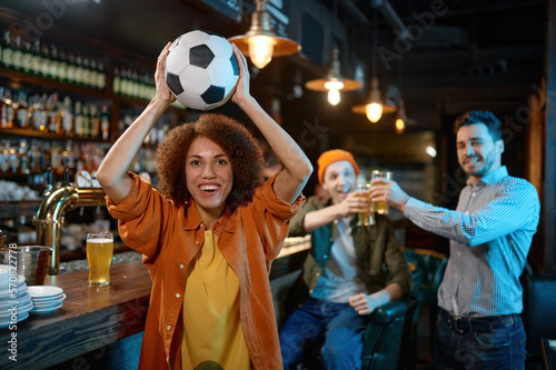 Happy friends rest at sports bar, focus on woman holding soccer ball