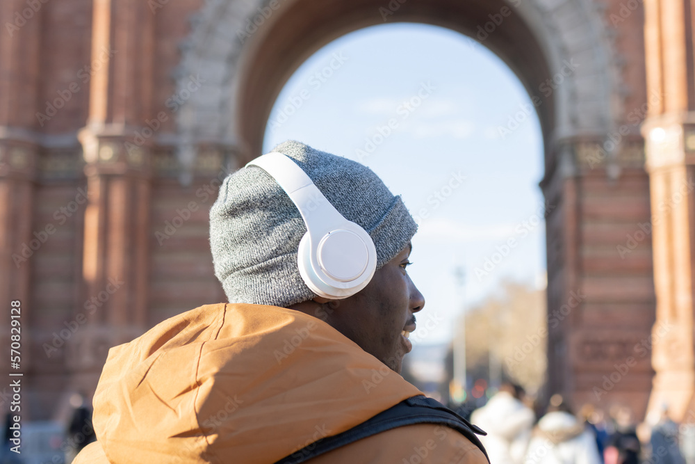 A man in winter vacation clothes wearing headphones in the city.