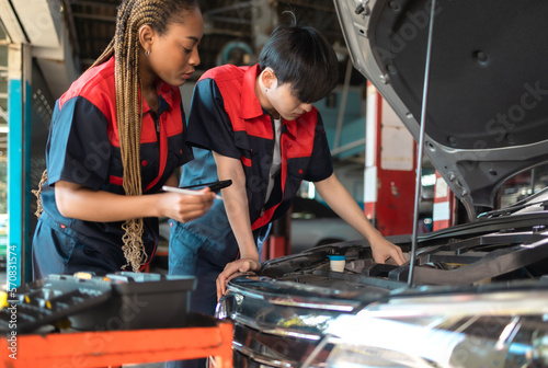 Auto service, repair, maintenance concept. Mechanic checks the car at the service station.African american woman  and asian engineer use tablet check car battery .
