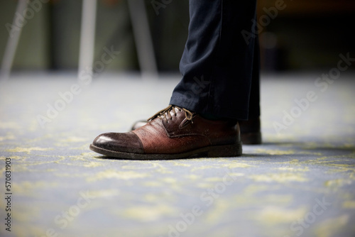 man in brown leather shoes indoors, legs close up. Expensive brown men's shoes close-up in blue pants. Close-up young man in elegant shoes indoors.