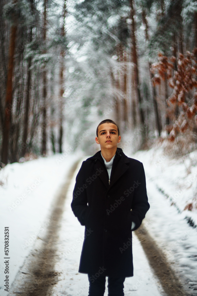 handsome young man is standing on a road covered with snow handsome young man is standing on a road covered with snow