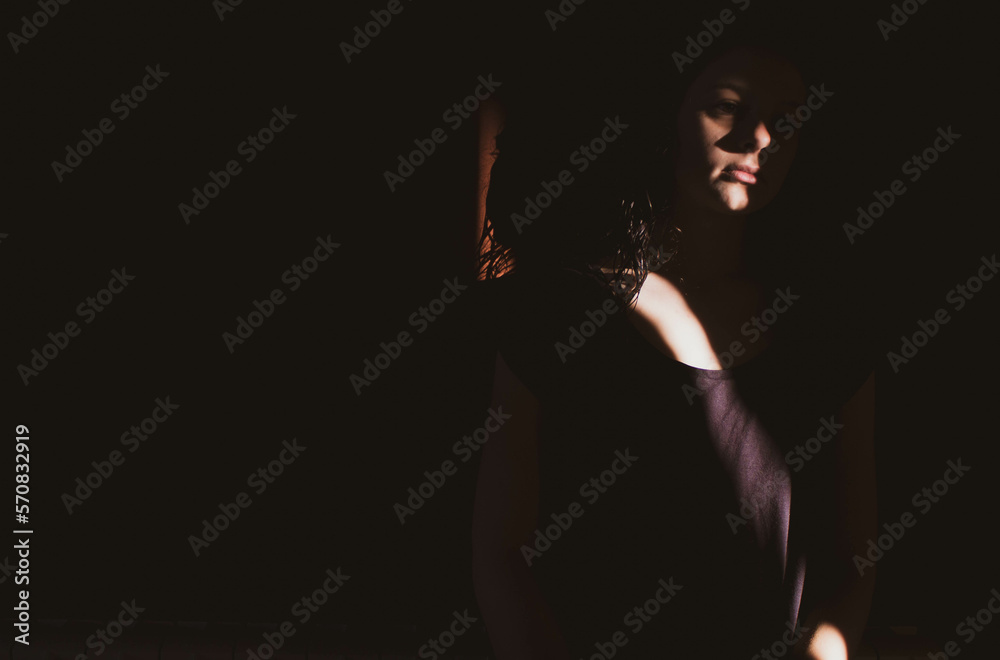 young woman on black background with light and shadow on sad face
