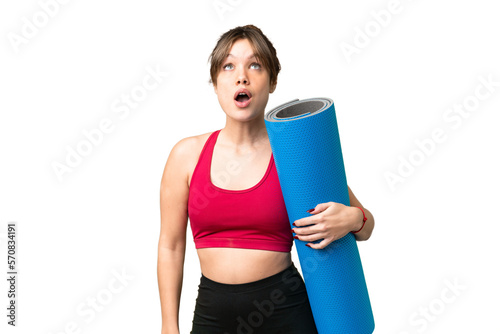Young sport girl going to yoga classes while holding a mat over isolated chroma key background looking up and with surprised expression
