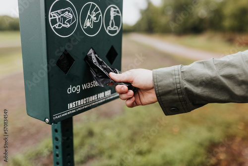 Adult female reaches for dog waste clean up bag while on walking trail