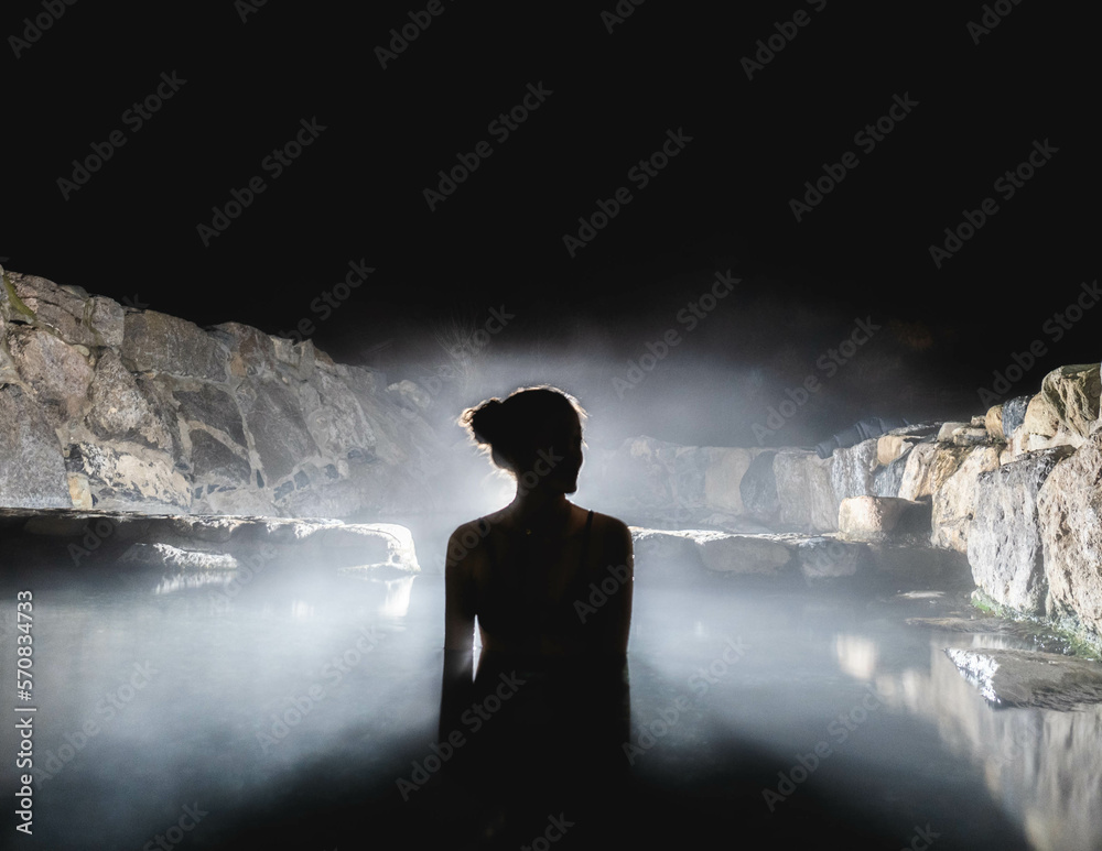 woman in natural hot springs at night with steam and backlight Stock