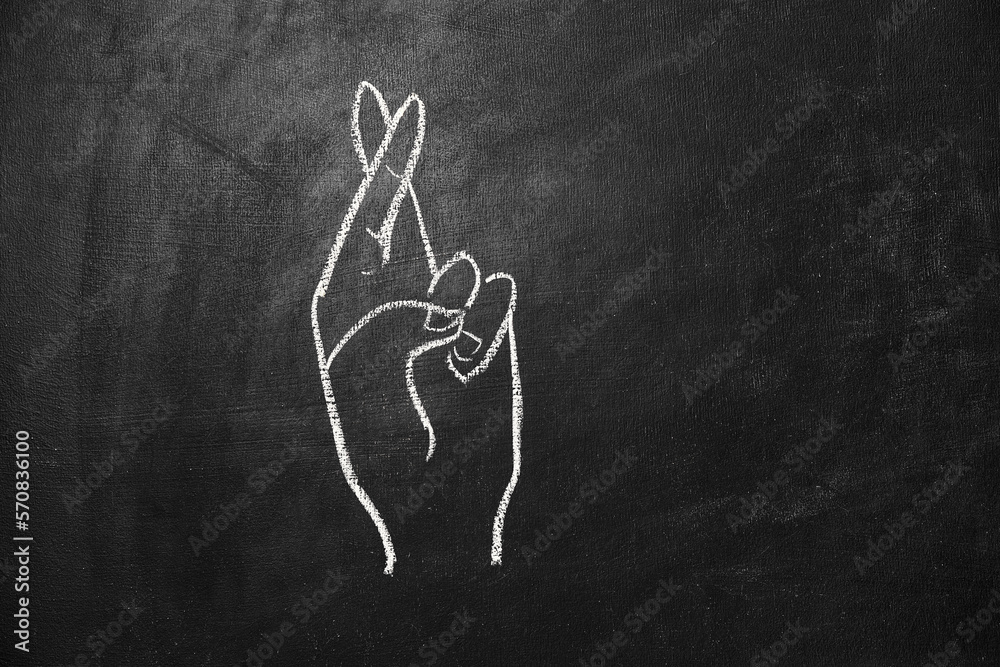 Hand with crossed fingers drawn in chalk on a black board