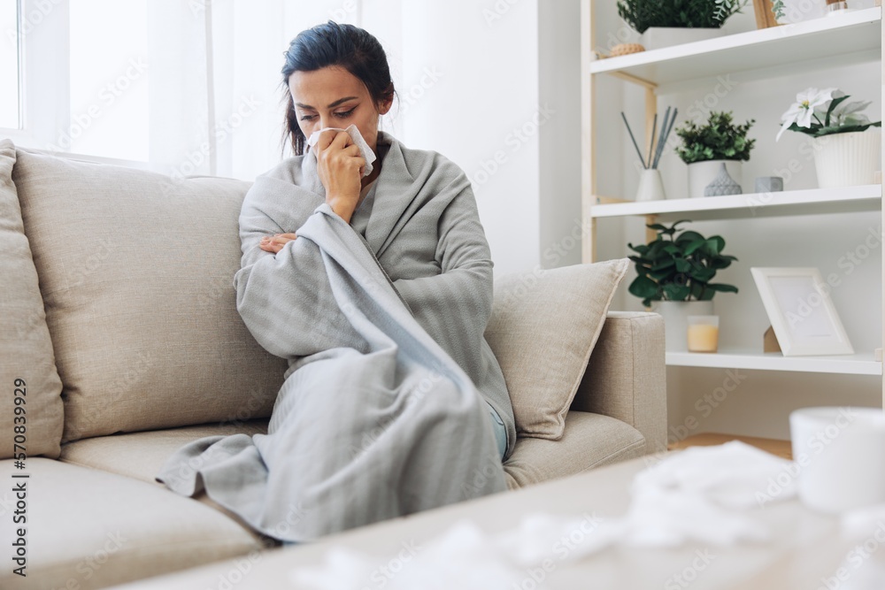 Woman cold headache runny nose and stuffy nose sitting on sofa in plaid, treatment for flu, allergies and covid-19 Woman cold headache runny nose and stuffy nose sitting on sofa in plaid, treatment for flu, allergies and covid-19
