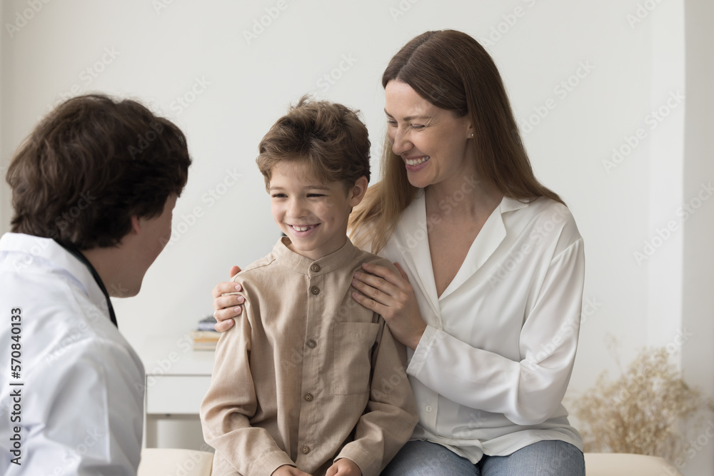 Cheerful boy and happy mom visiting pediatrician man for medical checkup, talking to doctor, smiling, laughing. Family practitioner meeting with patient kid and parent in office Cheerful boy and happy mom visiting pediatrician man for medical checkup, talking to doctor, smiling, laughing. Family practitioner meeting with patient kid and parent in office