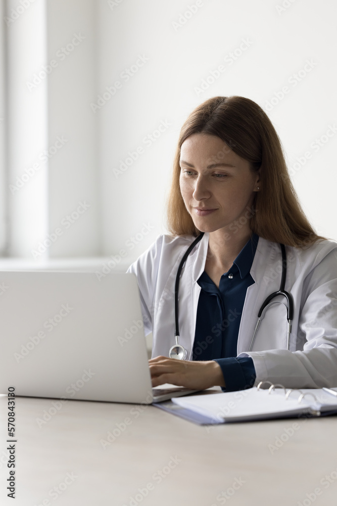 Positive beautiful practitioner woman using laptop computer at work table, chatting with patient online, using medical app for Internet communication, giving help, assistance. Vertical shot Positive beautiful practitioner woman using laptop computer at work table, chatting with patient online, using medical app for Internet communication, giving help, assistance. Vertical shot