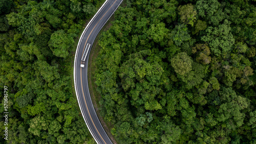 Aerial top view commercial gasoline fuel truck driving through the middle green forest, Gasoline fuel truck driving on the highway road between green forest, Tank truck on asphalt road through forest. © Kalyakan