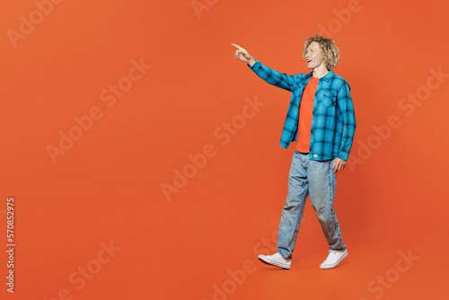 Full body young happy blond caucasian man wear blue shirt orange t-shirt point index finger aside on workspace area mock up isolated on plain red background studio portrait. People lifestyle concept.