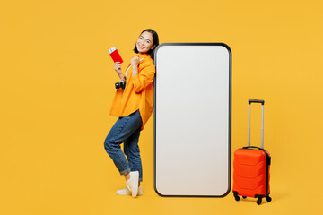 Young woman wear summer clothes stand near big huge blank screen mobile cell phone isolated on plain yellow background Tourist travel abroad in free time rest getaway. Air flight trip journey concept