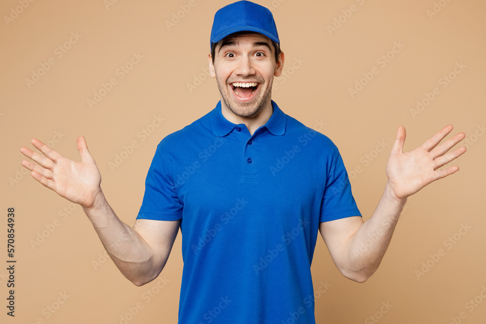 Professional excited delivery guy employee man wear blue cap t-shirt uniform workwear work as dealer courier look camera spread hands say wow isolated on plain light beige background. Service concept.