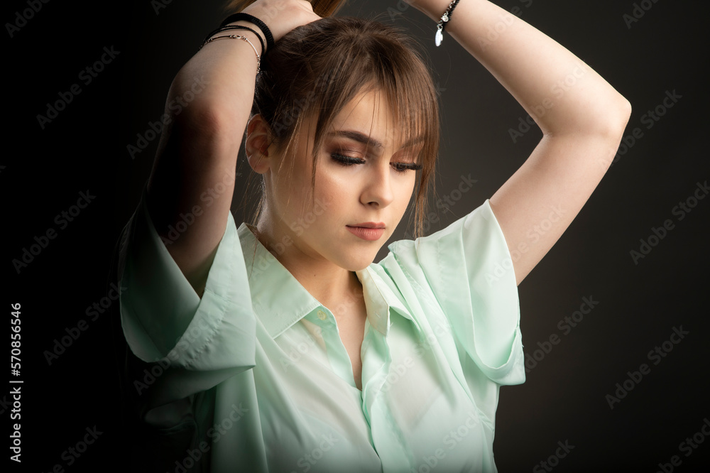 Portrait of a young girl fixing her hair in a studio on a dark background Portrait of a young girl fixing her hair in a studio on a dark background