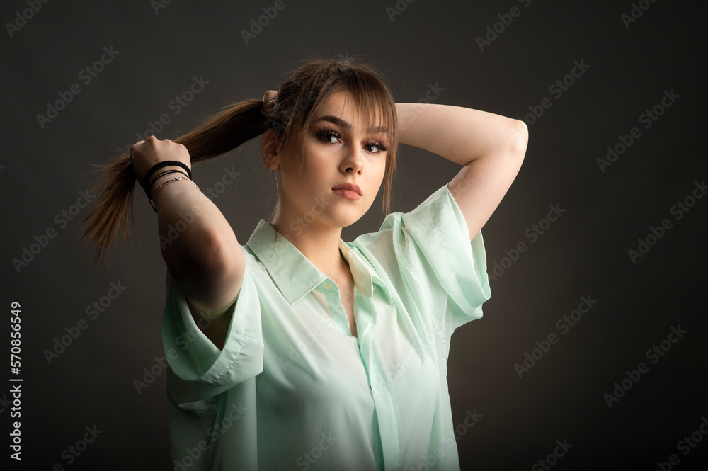Portrait of a young girl fixing her hair in a studio on a dark background Portrait of a young girl fixing her hair in a studio on a dark background