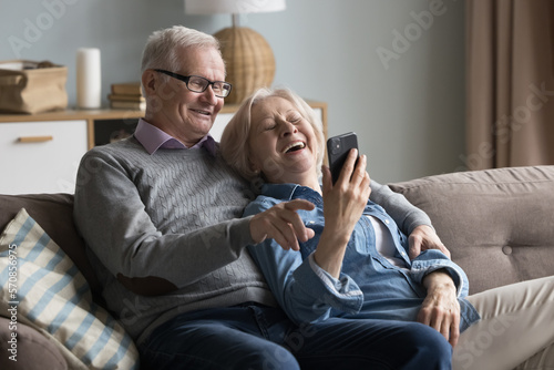 Joyful old husband and wife watching media on mobile phone, talking on video call together, smiling, laughing. Mature retired couple using online app for shopping, internet communication © fizkes