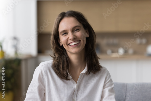Positive happy pretty young woman home head shot screen portrait. Cheerful adult girl looking at camera with toothy smile  sitting on couch  talking on video call  laughing