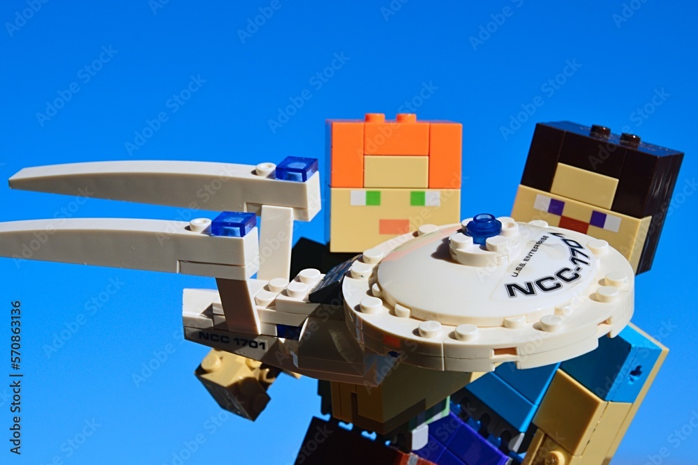 Naklejka premium LEGO Minecraft figures of Steve and Alex examining KREO model of Star Trek spaceship USS Enterprise, blue morning winter skies, daylight sunshine.
