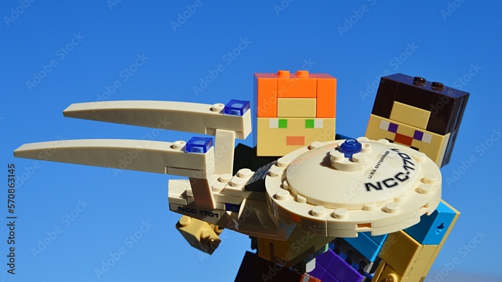 Fototapeta premium LEGO Minecraft figures of Steve and Alex as science fiction fans examining KREO model of Star Trek spaceship USS Enterprise, blue morning winter skies, daylight sunshine. 