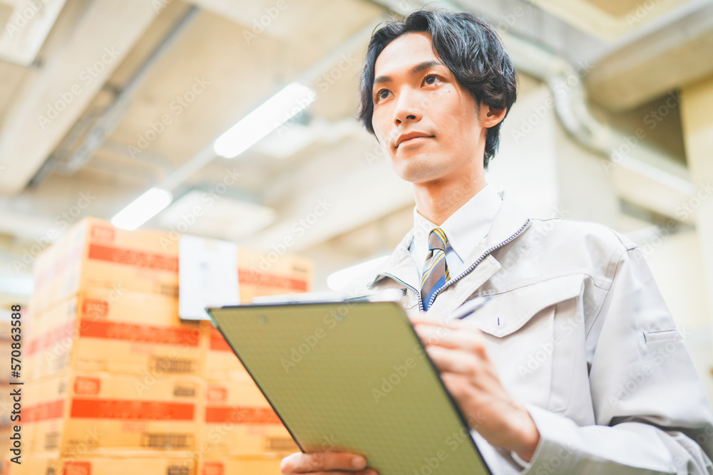 作業服を着て倉庫で在庫管理をする若いビジネスマン 作業服を着て倉庫で在庫管理をする若いビジネスマン