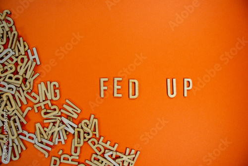FED UP in wooden English language capital letters spilling from a pile of letters on a orange background