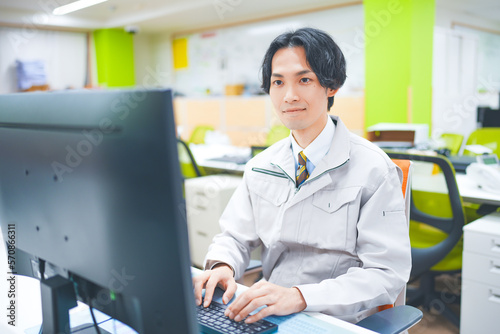 作業着を着てパソコン作業をする若いエンジニアの男性