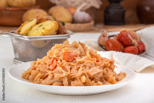 Stewed cabbage - bigos in a white porcelain plate against the background of pickled vegetables and baked potatoes. Close-up