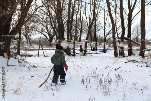 A boy in winter overalls walks in the evening near trees with blocks of ice after a winter flood
