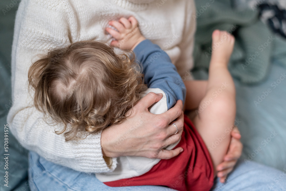 Mother breastfeeding baby, rear view. Woman with baby, mother gently hugs her child with both hands. She holds baby's bare foot in her hand. Mother breastfeeding baby, rear view. Woman with baby, mother gently hugs her child with both hands. She holds baby's bare foot in her hand.