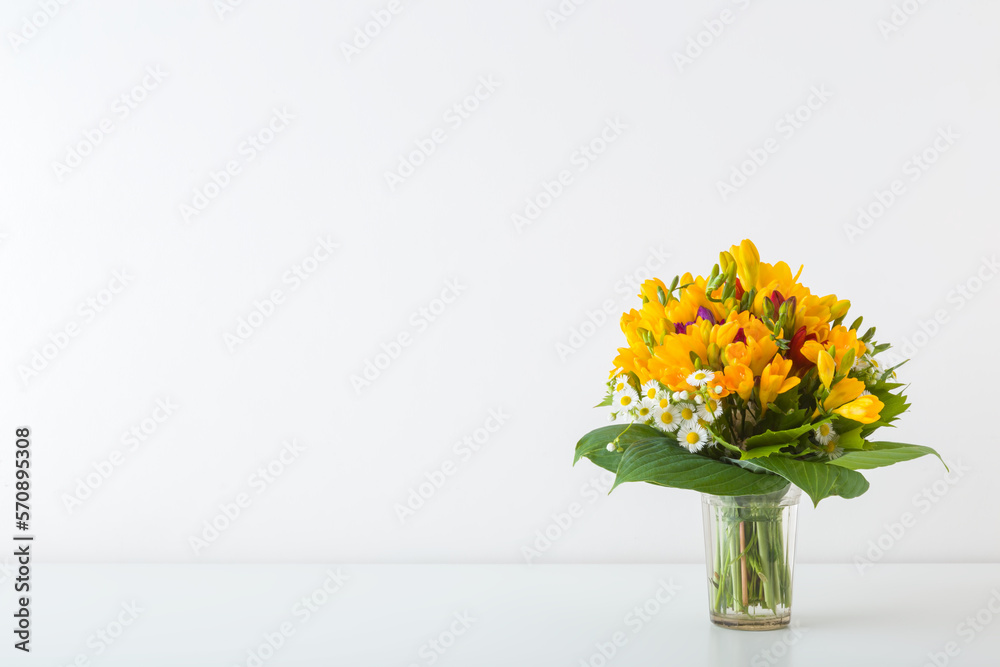 Beautiful fresh yellow freesia flower bouquet on white table at light gray wall background. Closeup. Empty place for inspirational text, lovely quote or positive sayings. Front view.