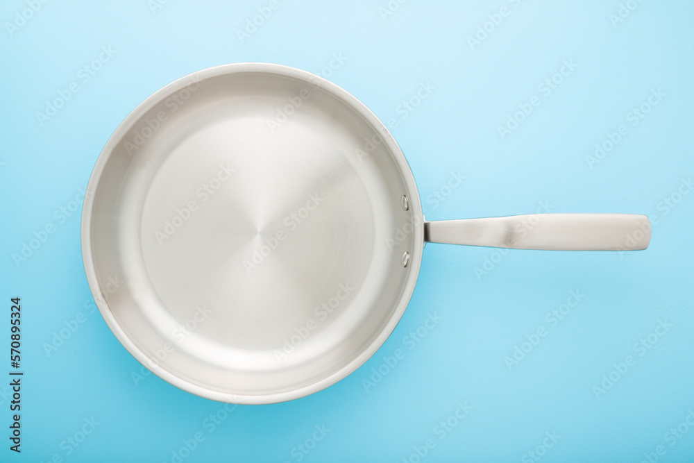 Empty new stainless frying pan on light blue table background. Closeup. Pastel color. Cooking concept. Top down view. Empty new stainless frying pan on light blue table background. Closeup. Pastel color. Cooking concept. Top down view.