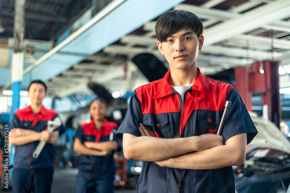 Fototapeta premium Asian automotive engineer people wear helmet work in mechanics garage.young auto mechanic in uniform is looking at camera and smiling examining car.
