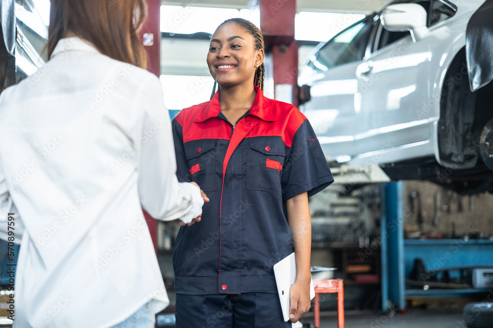 woman receiving her car keys.young african woman engineer auto mechanic in uniform is returning car key to a client, both are smiling. woman receiving her car keys.young african woman engineer auto mechanic in uniform is returning car key to a client, both are smiling.