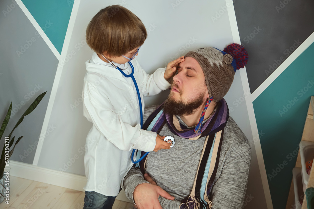 Father and child playing clinic and doctor, little boy in medical gown with stethoscope treats dad Father and child playing clinic and doctor, little boy in medical gown with stethoscope treats dad