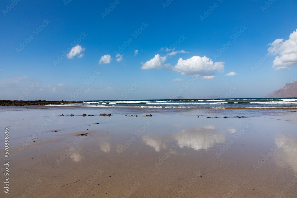 sandy beach at Famara in Lanzarote with reflection in water of clouds