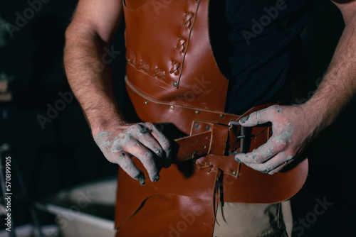 Man sculptor dress put on leather apron with clay in hands. Statue craft creation workshop.