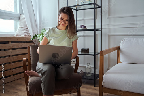 Young woman using laptop, typing, sitting in a chair, remote work, work at home
