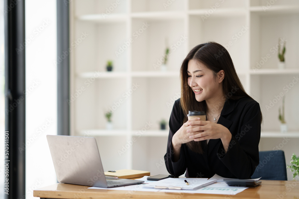 Happy Asian businesswoman working for her project and drinking coffee cup while working, sitting at the office desk.