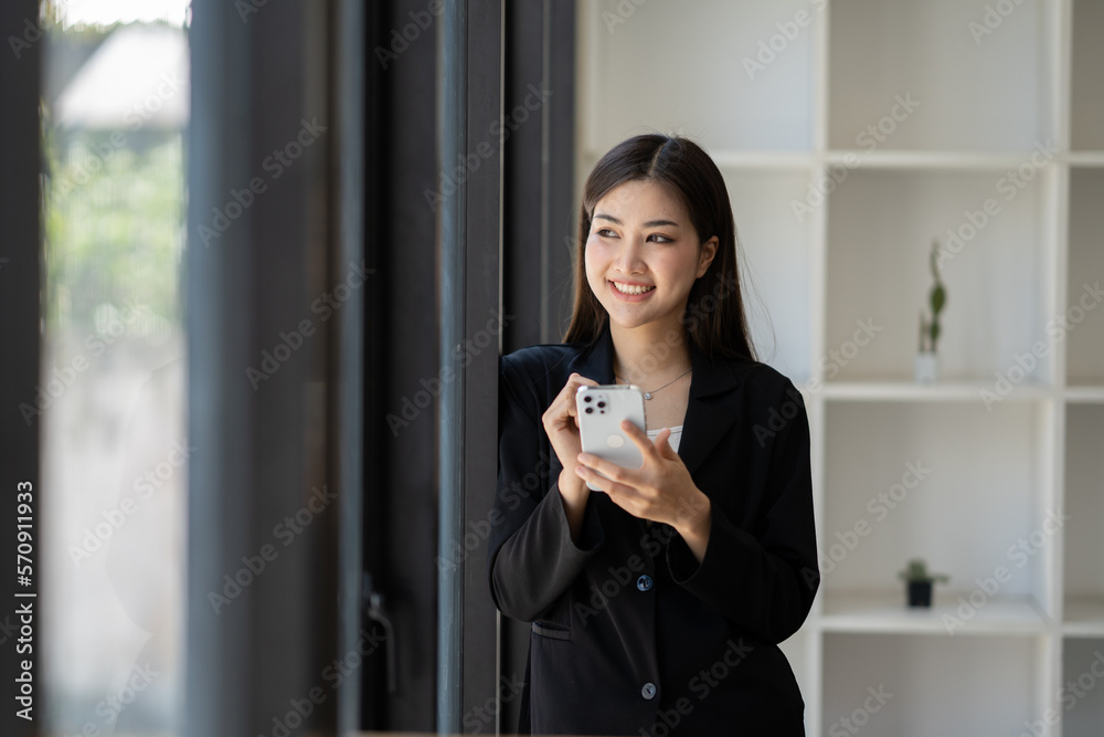 Portrait of young female businesswoman holding her smartphone while standing in the glass modern office room. Portrait of young female businesswoman holding her smartphone while standing in the glass modern office room.