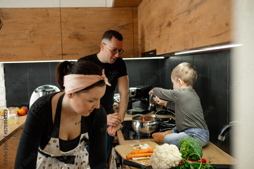Concentrated woman housewife, man, little blond boy cooking vegetable soup, salad in kitchen. Family household chores 