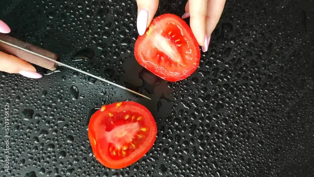 Ripe, red tomato cut into halves. Video where female hands cut a tomato. Cut vegetables on the board. Black background with drops and a wet tomato. Ripe, red tomato cut into halves. Video where female hands cut a tomato. Cut vegetables on the board. Black background with drops and a wet tomato.