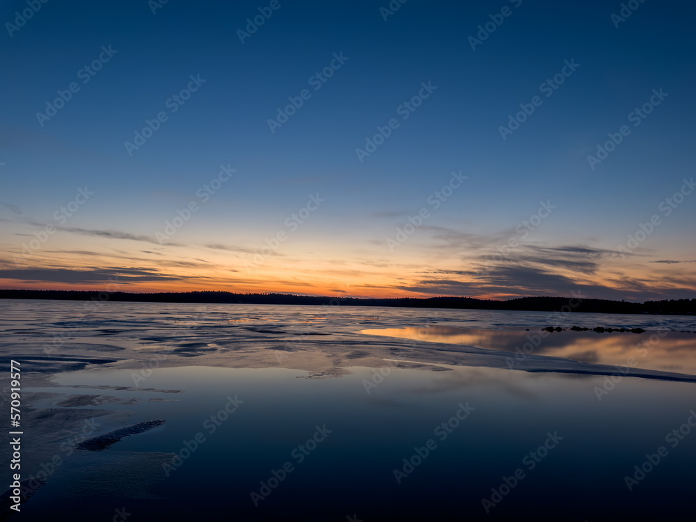 Scenic view of a frozen lake on a cold November night with a colorful sunset and the horizon in the background.