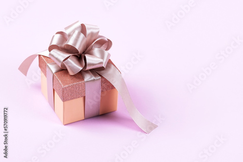 Lilac festive gift box with a satin ribbon bow on a lilac background. Happy Valentine's Day, Mother's Day and birthday greeting card.