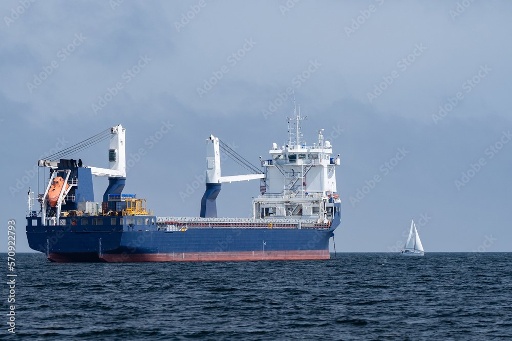 Huge cargo ship and small sailboat in the open sea. Concept of difference, diversity and distinction