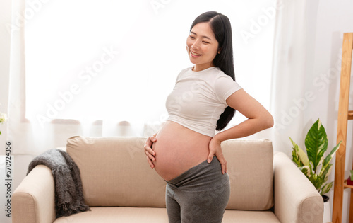Young asian beautiful pregnant woman holds hands on belly standing near window at home. Pregnancy, maternity, preparation and expectation concept. Free Download Young asian beautiful pregnant woman holds hands on belly standing near window at home. Pregnancy, maternity, preparation and expectation concept. - GFXLoad