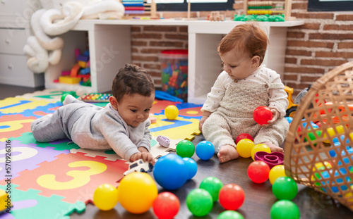 Two adorable babies playing with balls sitting on floor at kindergarten