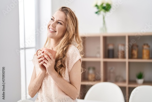 Young blonde woman smiling confident drinking coffee at home