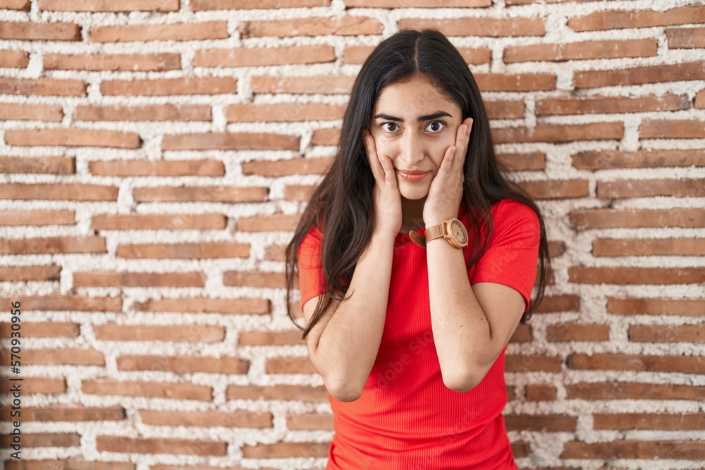 Young teenager girl standing over bricks wall tired hands covering face, depression and sadness, upset and irritated for problem