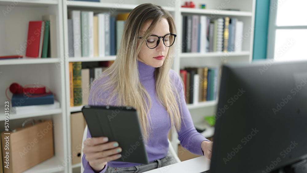 Young blonde woman student using computer and touchpad studying at library university Young blonde woman student using computer and touchpad studying at library university